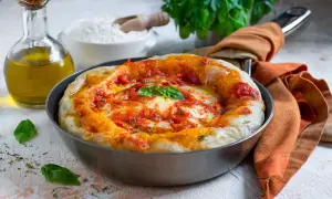 Pizza in padella appena sfornata, con pomodoro, mozzarella filante e basilico fresco. Accanto, olio d'oliva e farina, ingredienti per un'ottima pizza fatta in casa.
