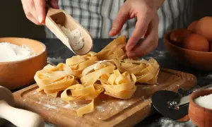 Mani che spolverano farina su nidi di pasta fatta in casa. Ingredienti freschi, uova e sale, pronti per un pasto delizioso.