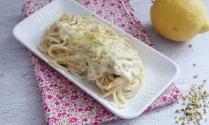 Un piatto di spaghetti al limone cremosi, guarniti con scorza di limone e pistacchi tritati, accanto a un limone intero.