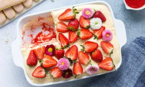 Tiramisù alle fragole ricetta originale: un dolce fresco e goloso, decorato con fragole fresche e piccoli fiori colorati.