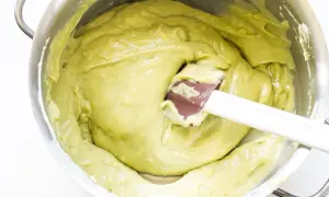 Una spatola mescola una densa crema al pistacchio in una ciotola d'acciaio.