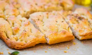 Focaccia senza lievito dorata e fragrante, tagliata a pezzi, con erbe aromatiche e un filo d'olio d'oliva.