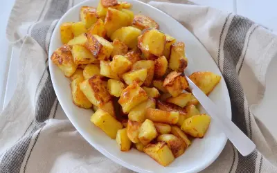 Un piatto bianco pieno di patate al forno dorate e croccanti, pronte per essere gustate.