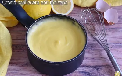 Crema pasticcera liscia e vellutata, preparata con amido di mais, pronta per farcire dolci. Accanto, limoni e frusta.