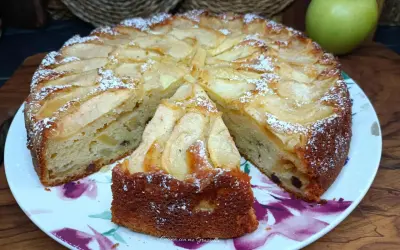Una fetta di torta di mele, cosparsa di zucchero a velo, su un piatto fiorato. Sullo sfondo, una mela verde.