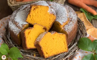 Una soffice torta di carote, cosparsa di zucchero a velo, servita in un cestino di vimini. Le fette mostrano l'interno arancione e invitante.