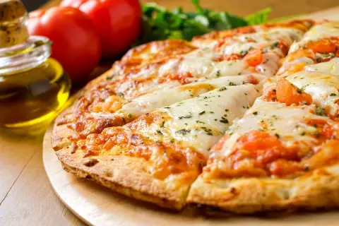 Pizza senza lievito dorata e filante, con pomodoro e mozzarella, accanto a pomodori freschi e olio d'oliva.