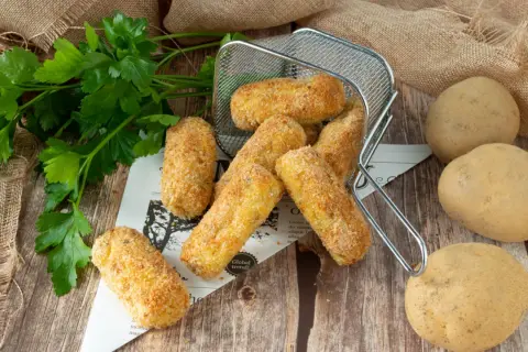 Crocchette di patate in friggitrice ad aria, dorate e croccanti, pronte per essere gustate. Accanto, patate fresche e prezzemolo.