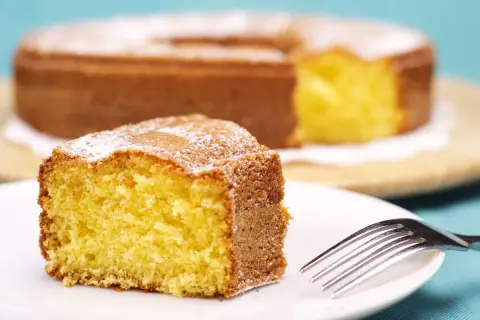 Una fetta di torta 7 vasetti soffice e dorata, spolverata di zucchero a velo, su un piatto bianco con una forchetta.