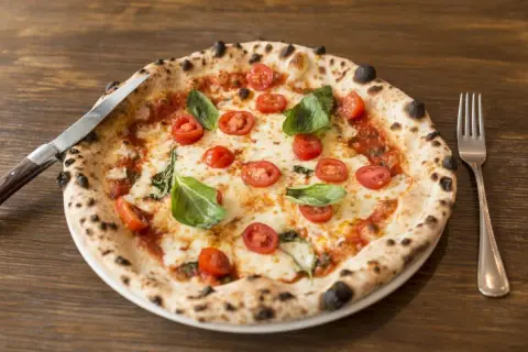 Pizza con lievito madre, pomodorini freschi, mozzarella filante e basilico profumato. Un capolavoro da gustare con coltello e forchetta.