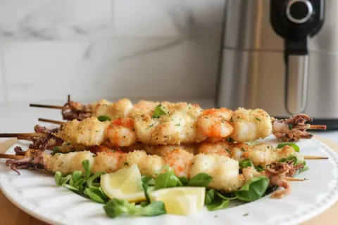 Spiedini di gamberi e calamari impanati, cotti alla perfezione nella friggitrice ad aria. Serviti su un letto di insalata con spicchi di limone.
