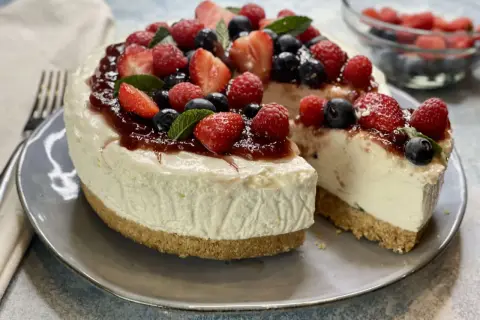 Deliziosa torta fredda allo yogurt, guarnita con fragole, lamponi, mirtilli e una cascata di marmellata. Perfetta per un dessert estivo.