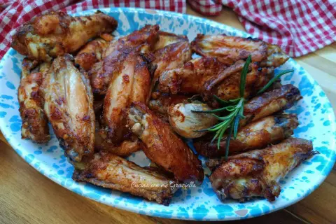 Alette di pollo al forno dorate e succulente, servite su un piatto decorato con un rametto di rosmarino.