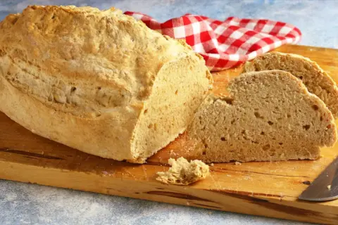 Pane casereccio con lievito istantaneo, tagliato su un tagliere di legno, con un tovagliolo a quadri rossi e bianchi.