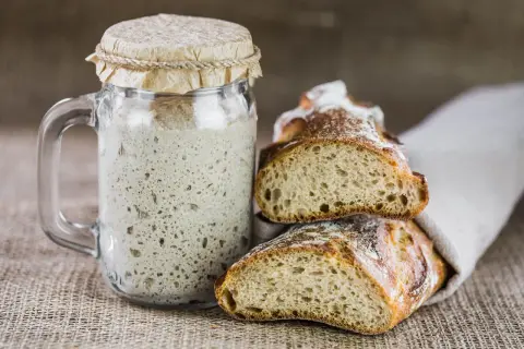 Un barattolo di lievito madre attivo e fette di pane rustico, pronti per creare deliziosi impasti. Ecco come si fa il lievito madre.