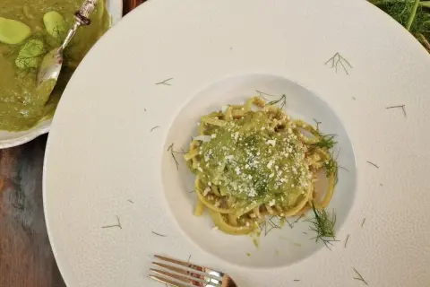 Un piatto di pasta condita con un cremoso macco di fave fresche, guarnito con aneto e formaggio grattugiato.