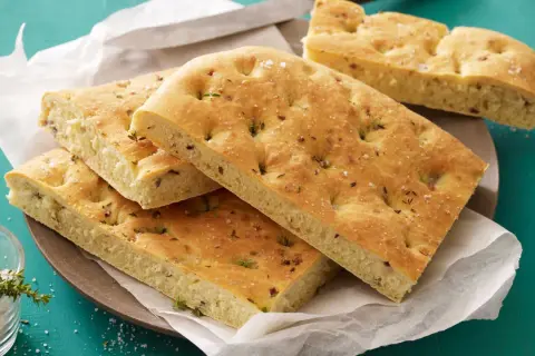 Focaccia con lievito istantaneo, dorata e soffice, guarnita con erbe aromatiche e sale grosso. Perfetta per un pasto veloce e gustoso.