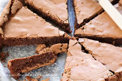 Una deliziosa torta al cioccolato fondente, tagliata a fette triangolari, con una crosta leggermente screpolata e un interno umido e invitante.
