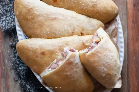 Calzoni al forno dorati e fragranti, ripieni di prosciutto e formaggio filante, pronti per essere gustati.