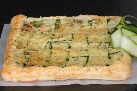 Torta salata con pasta sfoglia e zucchine, gratinata al forno e guarnita con fettine di zucchina fresca.