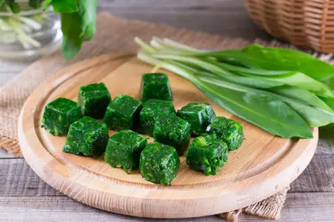 Cubetti di spinaci surgelati in padella, pronti per essere cucinati. Accanto, un mazzo di spinaci freschi.