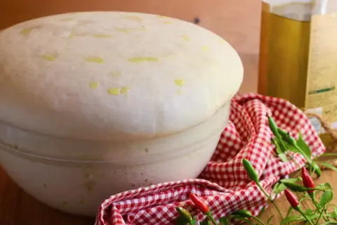 Impasto lievitato per pizza con lievito di birra, pronto per essere infornato. Olio d'oliva e peperoncini completano la scena.