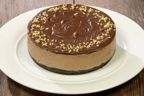 Cheesecake alla Nutella con glassa al cioccolato e nocciole tritate, su un piatto bianco.