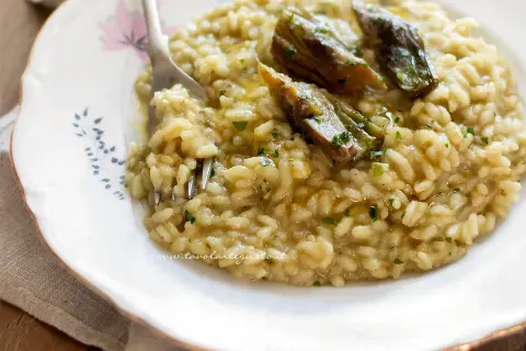 Un cremoso risotto con carciofi freschi, guarnito con prezzemolo tritato e un filo d'olio.