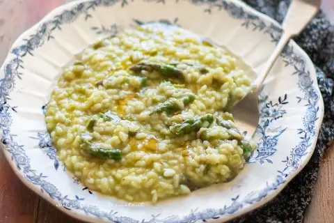 Un cremoso risotto con asparagi, servito su un piatto decorato. Un piatto primaverile che profuma di buono.