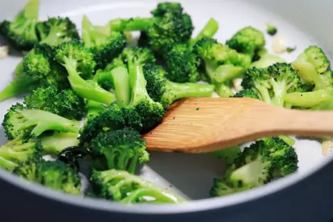 Broccoli in padella, con un mestolo di legno che mescola le cimette verdi e brillanti, pronte per essere gustate.