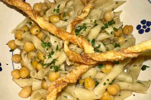 Piatto di ciceri e tria, pasta fresca con ceci e croccanti sfoglie fritte, guarnito con prezzemolo tritato.