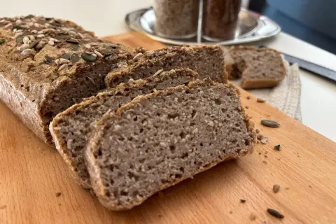 Fetta di pane di grano saraceno, cosparso di semi, su tagliere di legno.