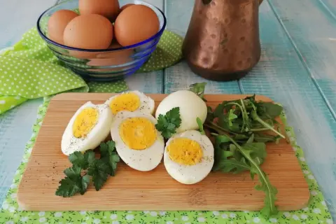Uova sode in friggitrice ad aria, tagliate a metà, con un ciuffo di prezzemolo e rucola su un tagliere di legno.