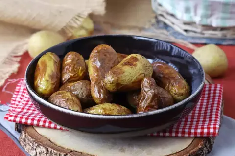 Patate novelle dorate e croccanti, appena sfornate dalla friggitrice ad aria, servite in una ciotola scura.