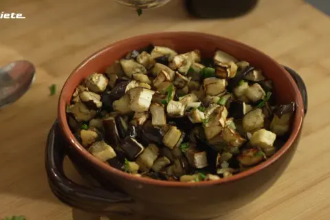 Melanzane in friggitrice ad aria, tagliate a cubetti e condite con erbe aromatiche, servite in una ciotola di terracotta.