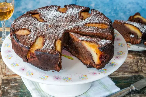 Torta al cioccolato e pere, cotta in friggitrice ad aria, spolverata di zucchero a velo. Una fetta è già servita.