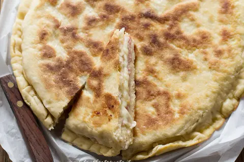 Focaccia in padella dorata e fragrante, farcita con formaggio e salumi, tagliata a spicchi.