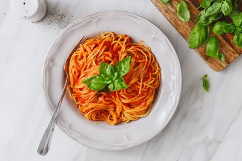 Un piatto di spaghetti al sugo di pomodorini freschi, guarnito con basilico, pronto per essere gustato.