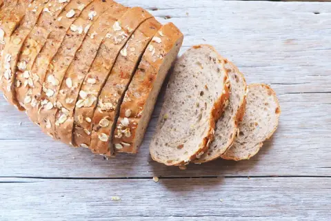 Pane fatto in casa ricetta della nonna, con crosta dorata e semi, affettato su un tavolo di legno.