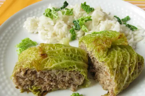 Involtini di verza ripieni di carne e riso, serviti su un piatto bianco con contorno di riso bianco e foglie di verza sminuzzate.