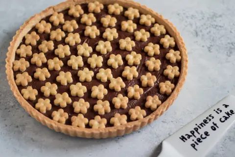 Deliziosa crostata alla nutella con decorazioni a forma di fiorellini. Un dolce che porta gioia, come dice la spatola: "Happiness is a piece of cake".