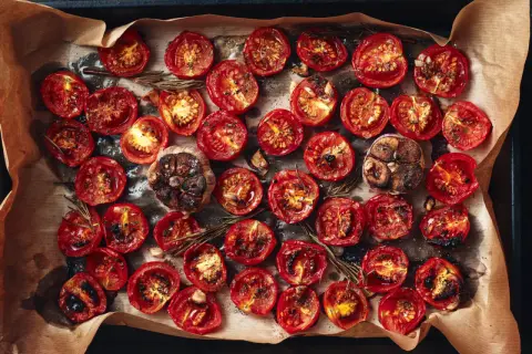 Pomodorini al forno, caramellati e profumati al rosmarino, con teste d'aglio arrostite.