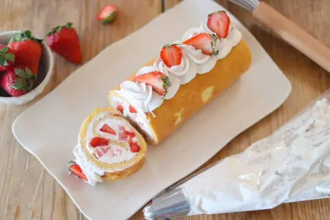 Rotolo panna e fragole decorato con panna montata e fragole fresche, pronto per essere gustato.
