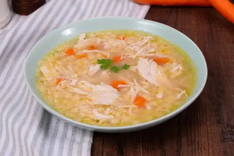 Un confortevole brodo di pollo con pezzi di pollo sfilacciato, carote e un rametto di prezzemolo.