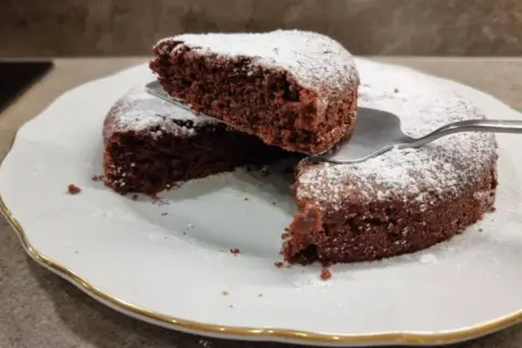 Una fetta di torta all'acqua al cacao, soffice e spolverata di zucchero a velo, viene sollevata da una spatola.