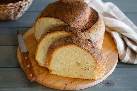 Pane di semola rustico, affettato su tagliere di legno, con coltello e tovagliolo a righe.