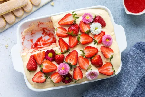 Tiramisù alle fragole ricetta originale: un dolce fresco e goloso, decorato con fragole fresche e piccoli fiori colorati.