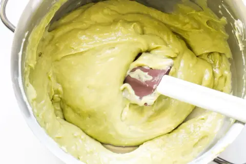 Una spatola mescola una densa crema al pistacchio in una ciotola d'acciaio.