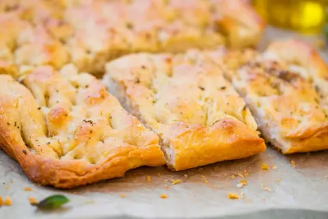 Focaccia senza lievito dorata e fragrante, tagliata a pezzi, con erbe aromatiche e un filo d'olio d'oliva.