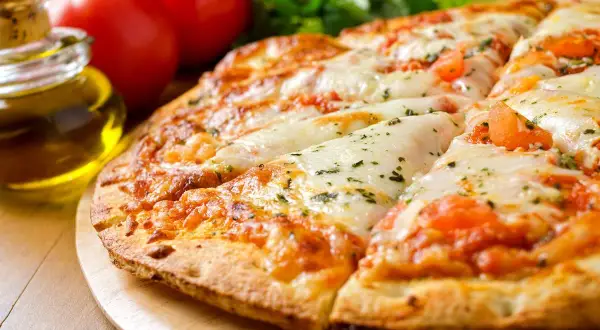 Pizza senza lievito dorata e filante, con pomodoro e mozzarella, accanto a pomodori freschi e olio d'oliva.